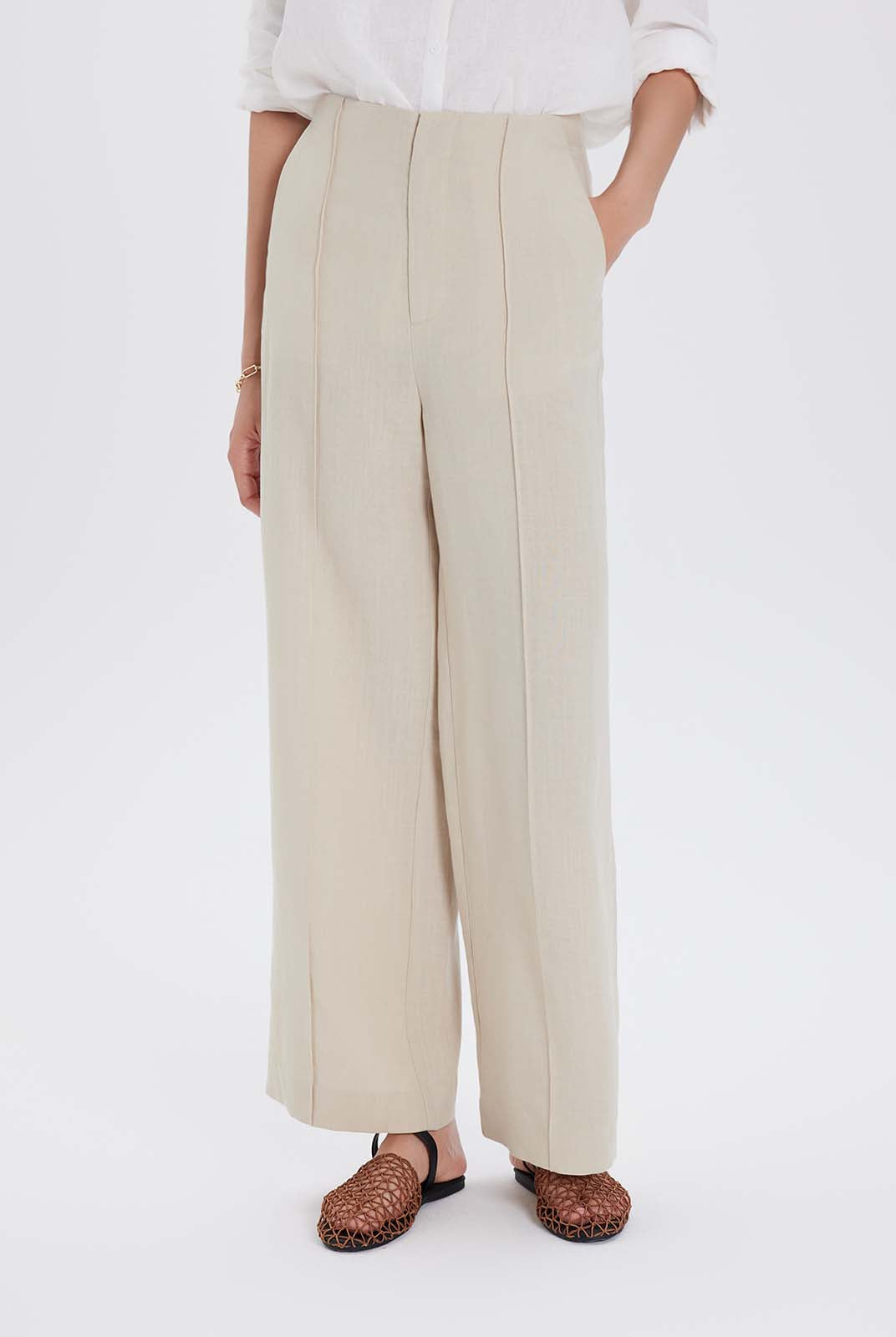 Person wearing beige wide-leg pants and a white top on a white background