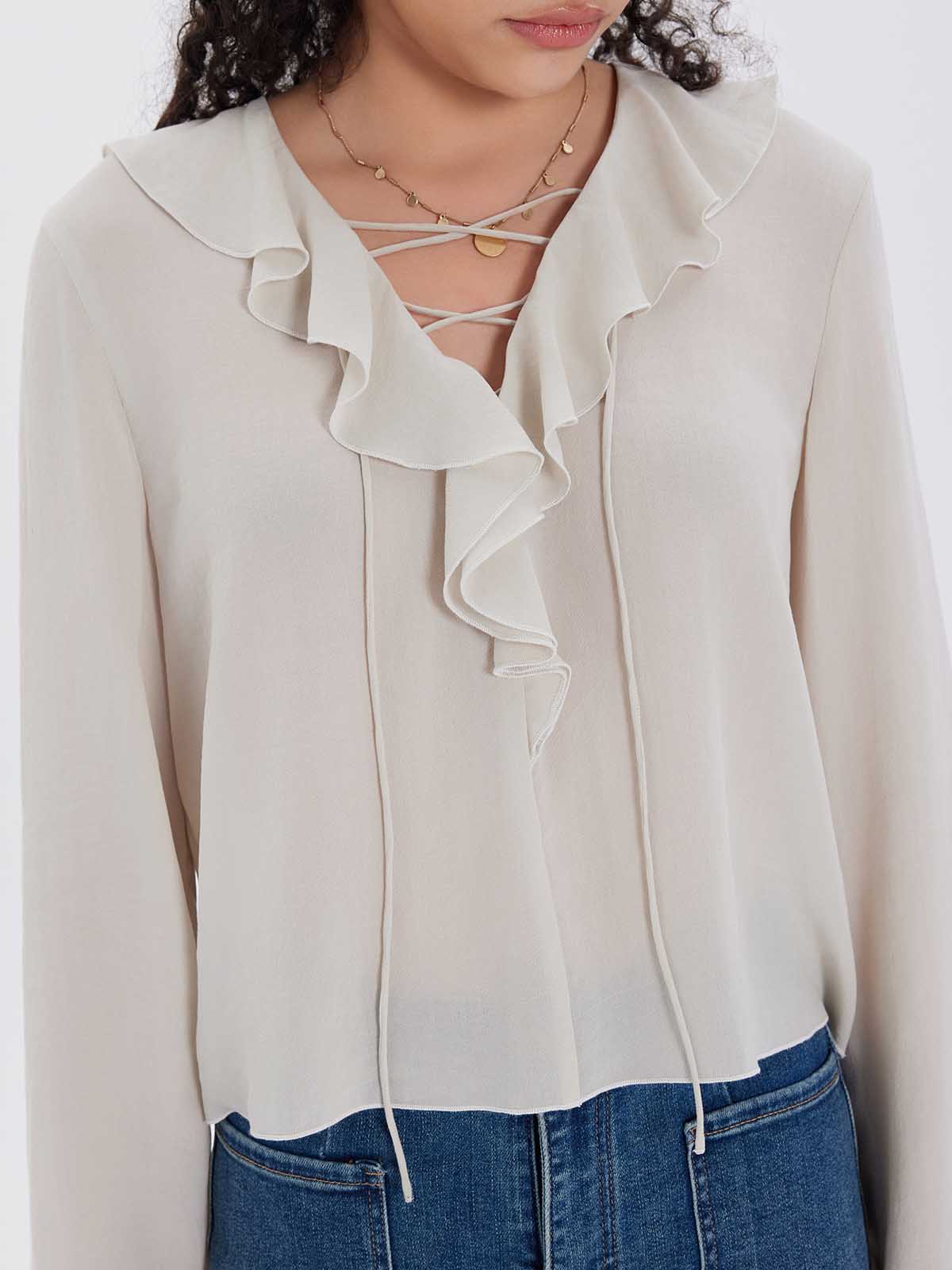 Woman wearing a light-colored blouse with ruffled collar and blue jeans